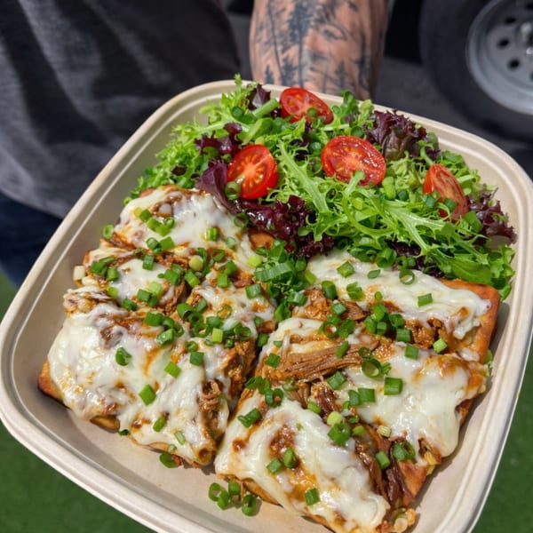 A person holds a takeout container with cheesy flatbread and a side salad with cherry tomatoes.